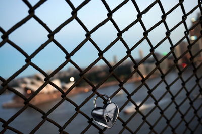 Close-up of heart shape padlock on chainlink fence against sky