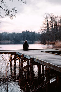 Rear view of woman sitting by lake against sky