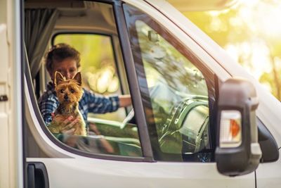 Woman holding dog looking through vehicle window