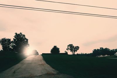 Road by trees against sky during sunset