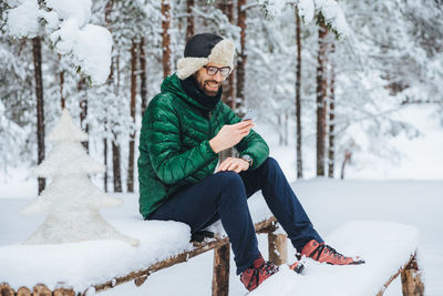 Young man sitting on snow covered tree