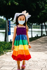 Little girl wearing face mask with rainbow dress enjoying outdoor in the park. new normal.