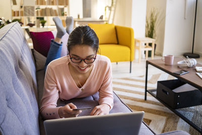 Young woman with credit card doing online shopping on laptop at home