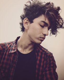 Young man with messy hair looking away against wall