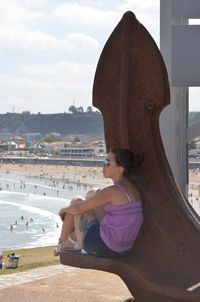 Woman sitting on rusty metal over sea against sky