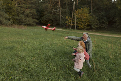 Grandfather and grandchildren playing with airplane toy on grass