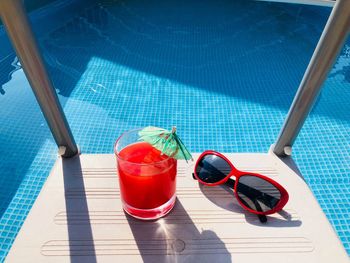 Red sunglasses and a glass of blood orange juice with a small umbrella on the stairs of a pool