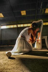 Rear view of woman applying make-up in front of mirror in empty warehouse