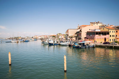 Sailboats moored in harbor by buildings against clear blue sky