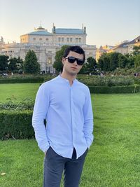 Young man wearing sunglasses standing by grass against sky