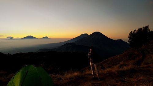 Man standing on land against sky during sunset