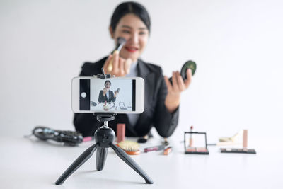 Young woman blogging through smart phone while holding beauty products