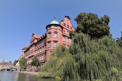 Low angle view of building by river against clear blue sky