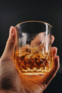 Cropped hand holding drink against black background