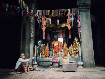 Full length of senior man praying by buddha statue at angkor wat