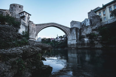 Arch bridge over river amidst buildings against sky