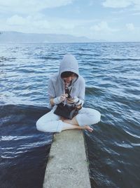 Woman using mobile phone while sitting on rock in river