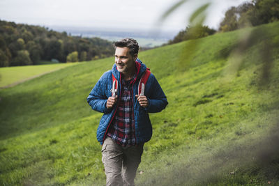 Happy mature man walking with backpack on meadow