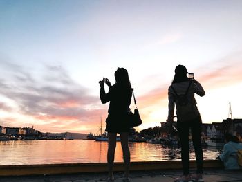 Silhouette woman photographing at camera against sky during sunset