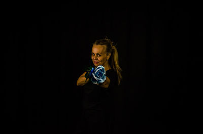 Portrait of senior woman holding rose against black background