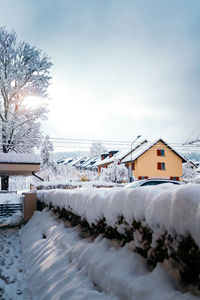 Snow covered houses by building against sky