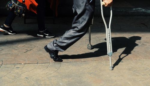 Low section of disabled man walking with help of canes on footpath
