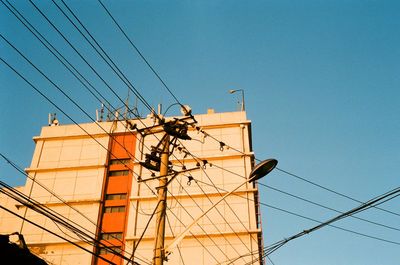 Low angle view of electricity pylon against building against clear blue sky