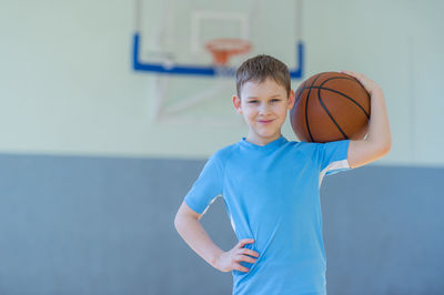 Portrait of boy holding basketball standing at court