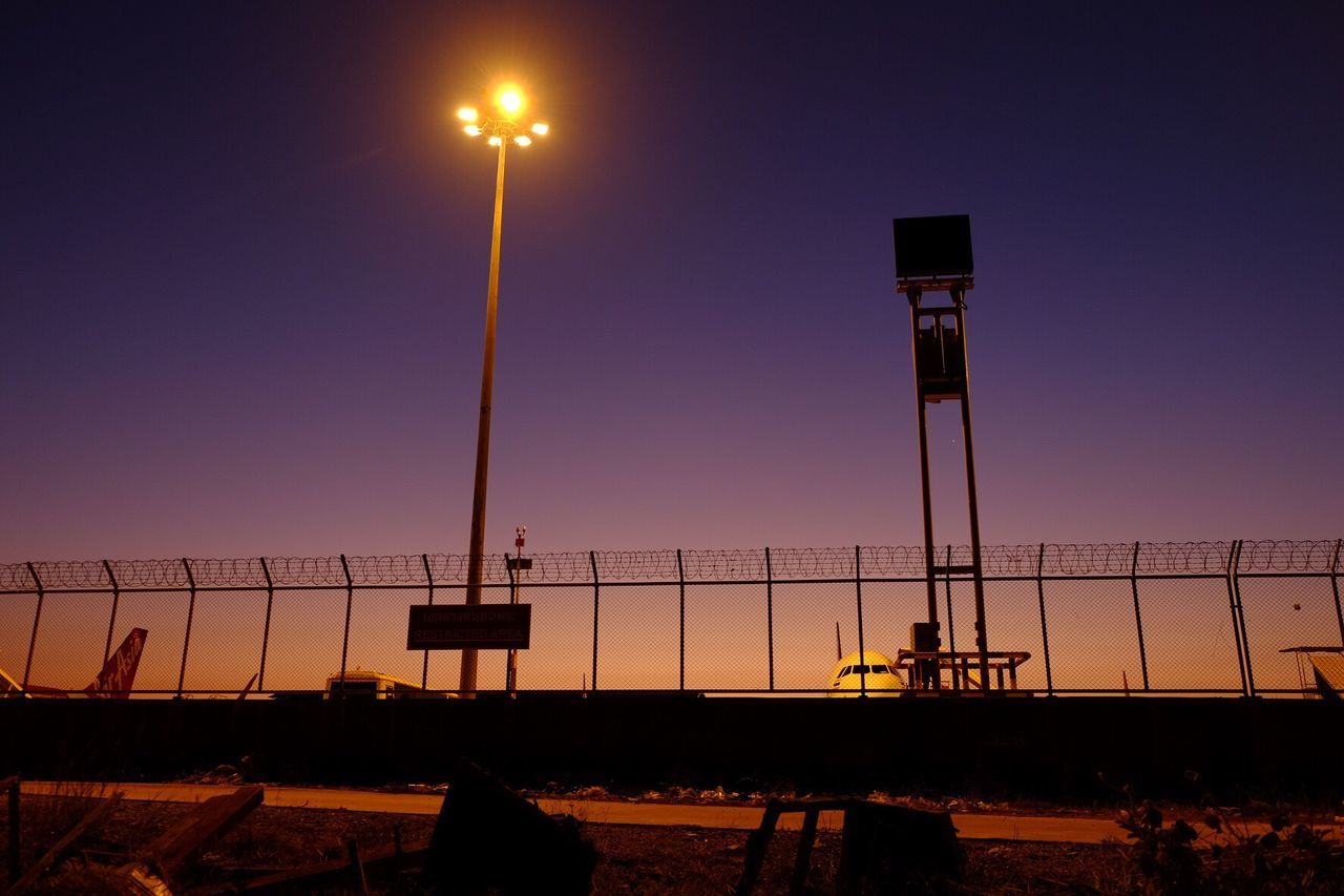street light, lighting equipment, illuminated, clear sky, copy space, sunset, transportation, low angle view, night, sky, lamp post, silhouette, dusk, electric light, pole, in a row, outdoors, blue, mode of transport, built structure