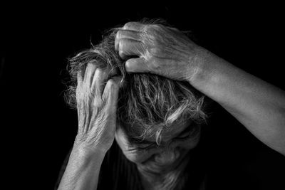 Close-up of senior woman with hands in hair against black background