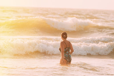 Rear view of woman standing at beach against sky during sunset