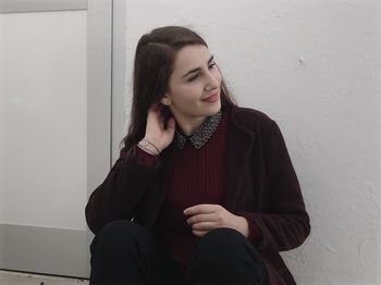Smiling young woman sitting against wall