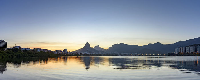 Scenic view of lake by buildings against sky during sunset