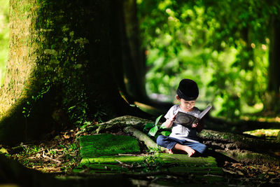 Boy sitting on plant against trees