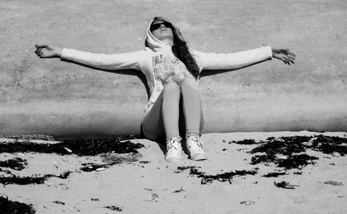 Young woman with arms outstretched leaning on wall at beach