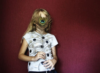 Girl holding peacock feather against wall