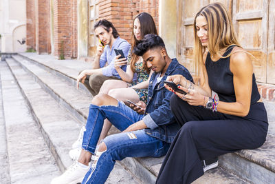 Friends using smart phone while sitting on steps outdoors