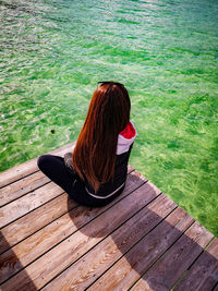 Rear view of woman sitting on pier over sea
