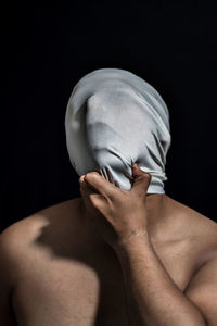 Shirtless man covering face with t-shirt against black background