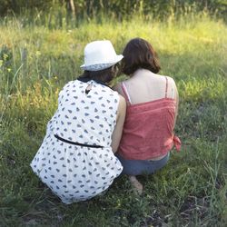 Rear view of female friends sitting on grassy field
