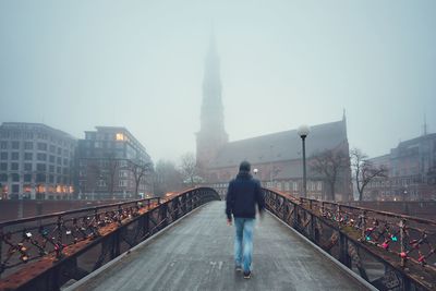 Rear view of man walking on bridge in city