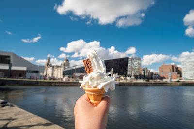 Midsection of person holding ice cream cone against sky