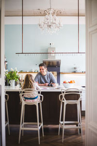 Smiling father looking at girl studying while sitting by kitchen island