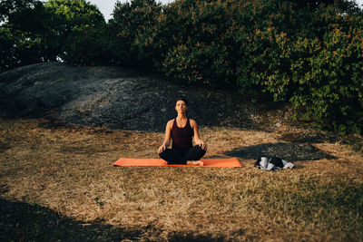 Full length of young woman practicing yoga on field in park