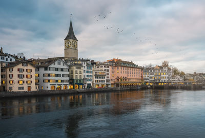 Buildings by river against cloudy sky