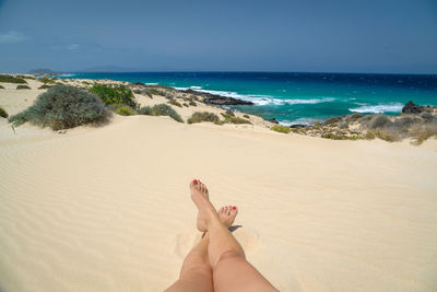 Low section of woman relaxing on sand at beach against sky