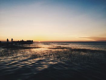 Silhouette people in sea against sky during sunset