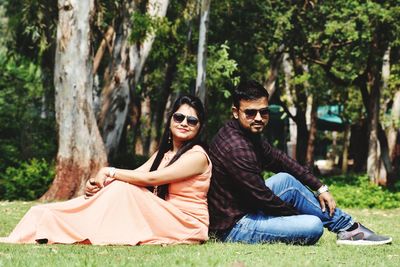 Side view of smiling young couple sitting on field at park