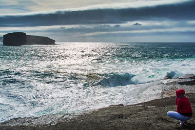 People on rocks by sea against sky