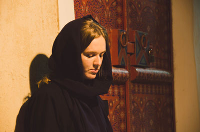 Portrait of young woman looking away while standing against door